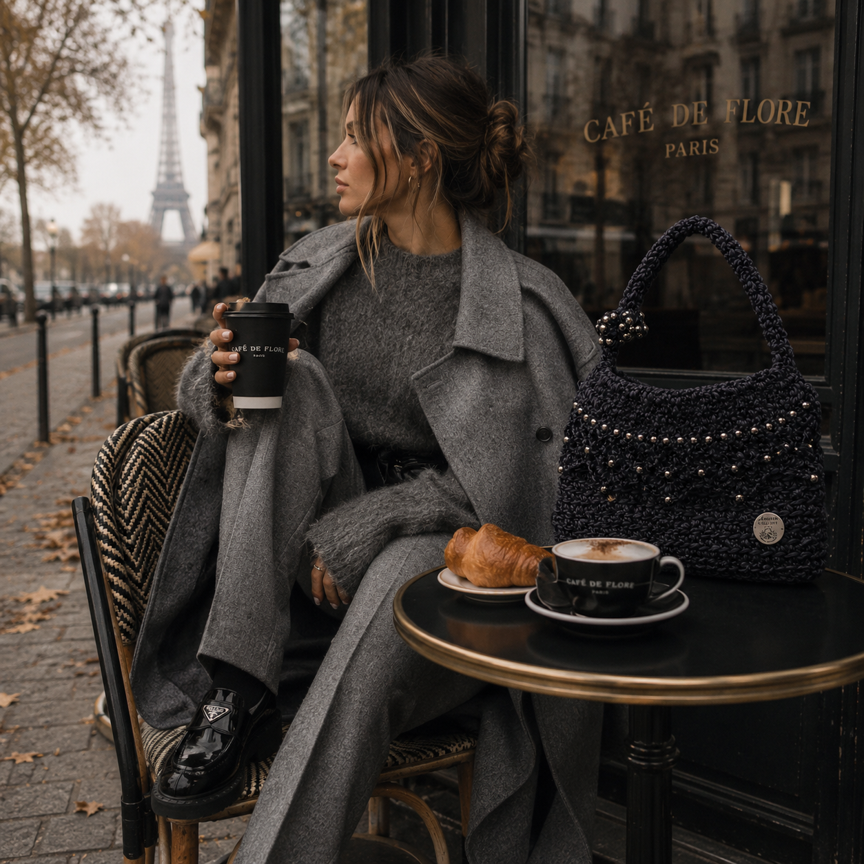 Mujer disfrutando un café en París con el bolso Eclipse Urbano de Amaro Crochet, tejido completamente a mano en crochet, combinado con un look elegante para un viaje de otoño o invierno.